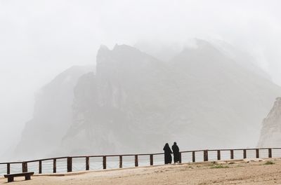 Two arabic women walking on the shore. foggy mountains in background. mughsayl / mughsail in oman.