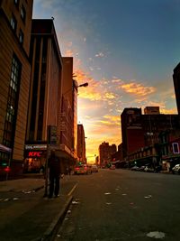 Street amidst buildings in city against sky during sunset