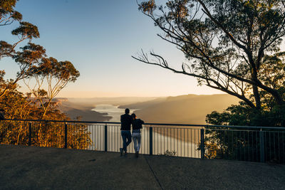 Rear view of people standing on railing against sky