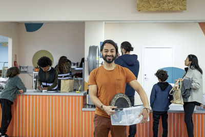 Portrait of smiling male customer holding container at recycling center