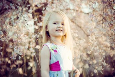 Portrait of smiling girl standing against cherry blossom at park