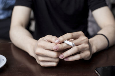 Close-up of man holding cigarette while sitting at table