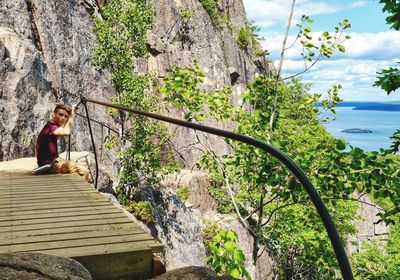 Woman standing on cliff by river against sky