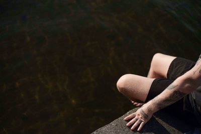 Low section of man sitting by lake