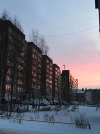 Snow covered buildings against sky during sunset