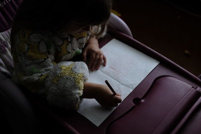 High angle view of girl writing on book at home