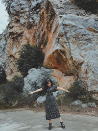 Portrait of woman in black dress standing in front of rock mountain 