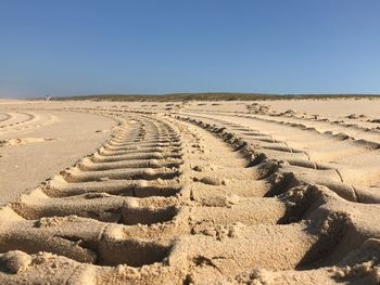 Tire tracks on sand dune against clear sky