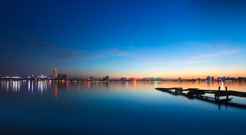 Illuminated city by sea against blue sky