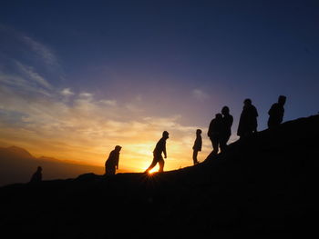 Silhouette people on land against sky during sunset