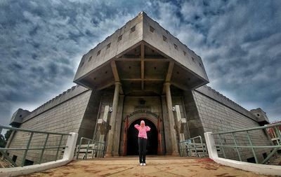 Low angle view of woman walking on building against cloudy sky