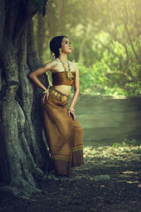 Full length of young woman looking away while standing by tree