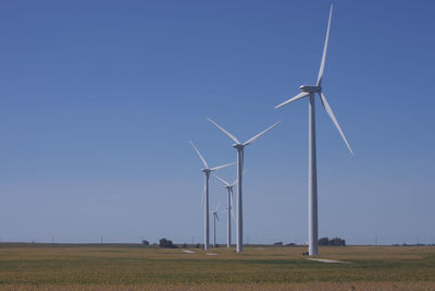 Low angle view of wind turbines on field against clear blue sky