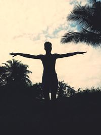 Rear view of silhouette person standing by tree against sky