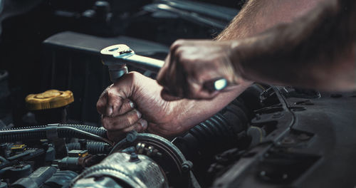 Cropped hands of mechanic repairing engine of car