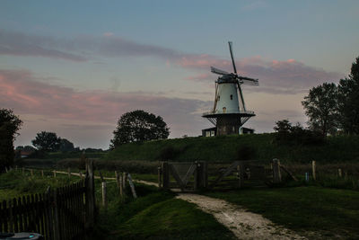 Traditional windmill on field against sky during sunset