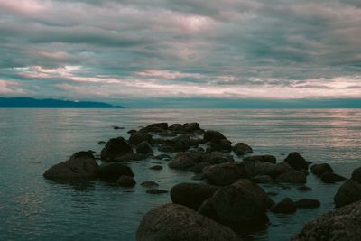 Rocks on sea shore against sky during sunset