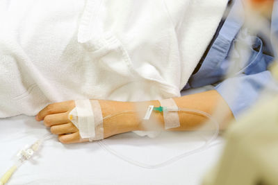 Midsection of woman with iv drip lying on bed in hospital