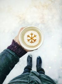 Low section of man holding coffee cup while standing on snow covered field