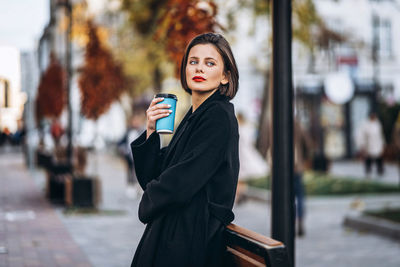 Portrait of young woman holding smart phone in city