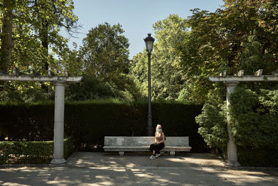 Woman in mask sitting on bench in park