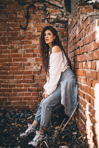 Portrait of young woman standing against brick wall