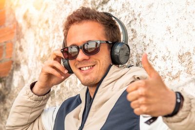 Portrait of young man wearing headphones gesturing by wall