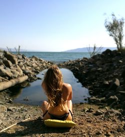 Rear view of bikini woman sitting at beach against clear sky