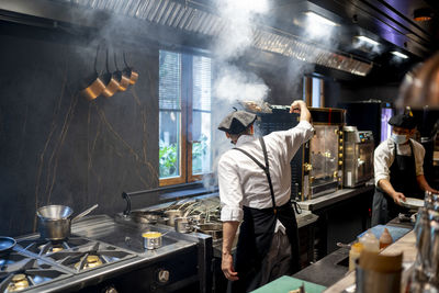 Chefs wearing protective face mask cooking dish in restaurant kitchen