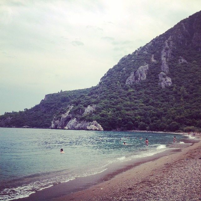 water, sea, beach, tranquil scene, scenics, tranquility, shore, beauty in nature, mountain, sky, nature, sand, rock formation, coastline, rock - object, incidental people, cliff, vacations, idyllic, day