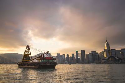 Ship in sea against buildings during sunset