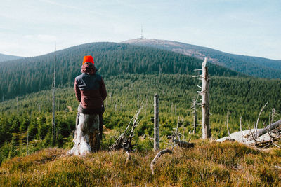 Rear view of woman sitting on tree stump against sky