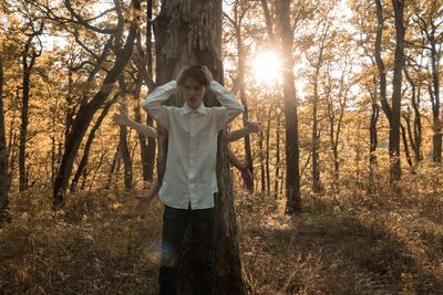 Worried man standing against tree trunk while hands gesturing behind him in forest