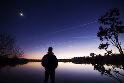 Silhouette man standing by lake against sky at night
