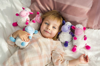 Portrait of smiling girl with toys lying on bed at home