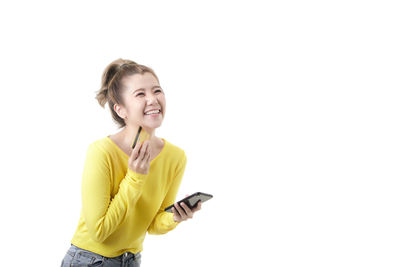 Young woman using phone while standing against white background