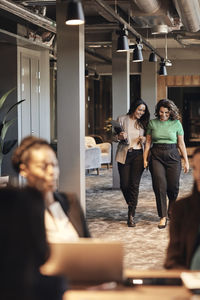 Happy female entrepreneurs walking and talking in office