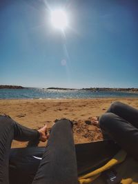 Low section of men sitting on beach against clear sky