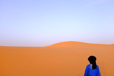 Rear view of man standing at desert against clear blue sky
