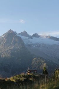 A young woman sitting in front of the snowy swiss mountains, admiring the scenic view.