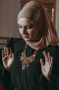 Close-up of young woman wearing hijab praying indoors