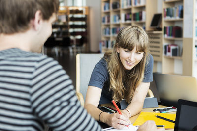 Young woman with male friend studying together in university library