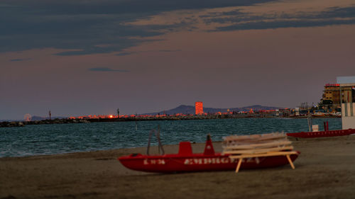 Boat moored on beach against sky during sunset