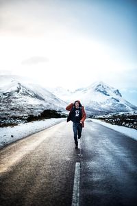 Full length rear view of man walking on snowcapped mountain