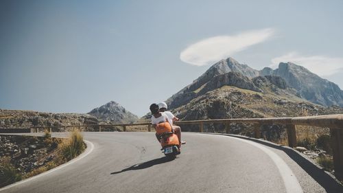 Man riding motorcycle on road against mountain range