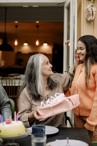 Smiling granddaughter giving birthday present to grandmother at patio