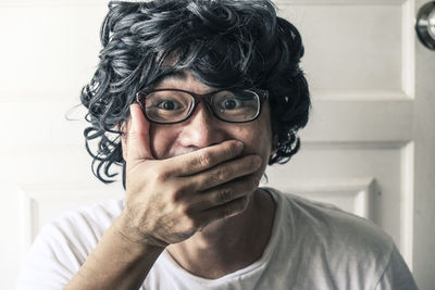 Portrait of man covering mouth with hands at home