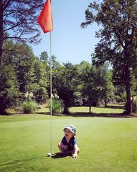 Cute baby boy sitting by golf flag on field