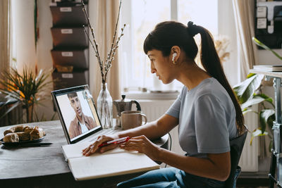 Side view of female freelancer doing video call with male colleague through laptop at home office