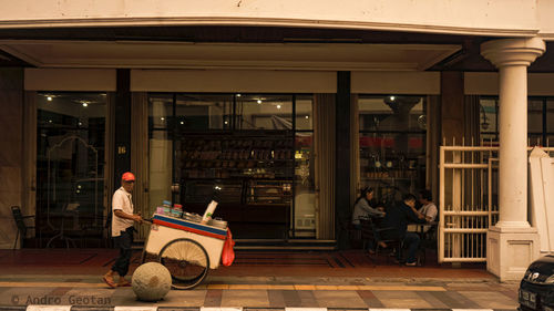 Man sitting on street against building at night